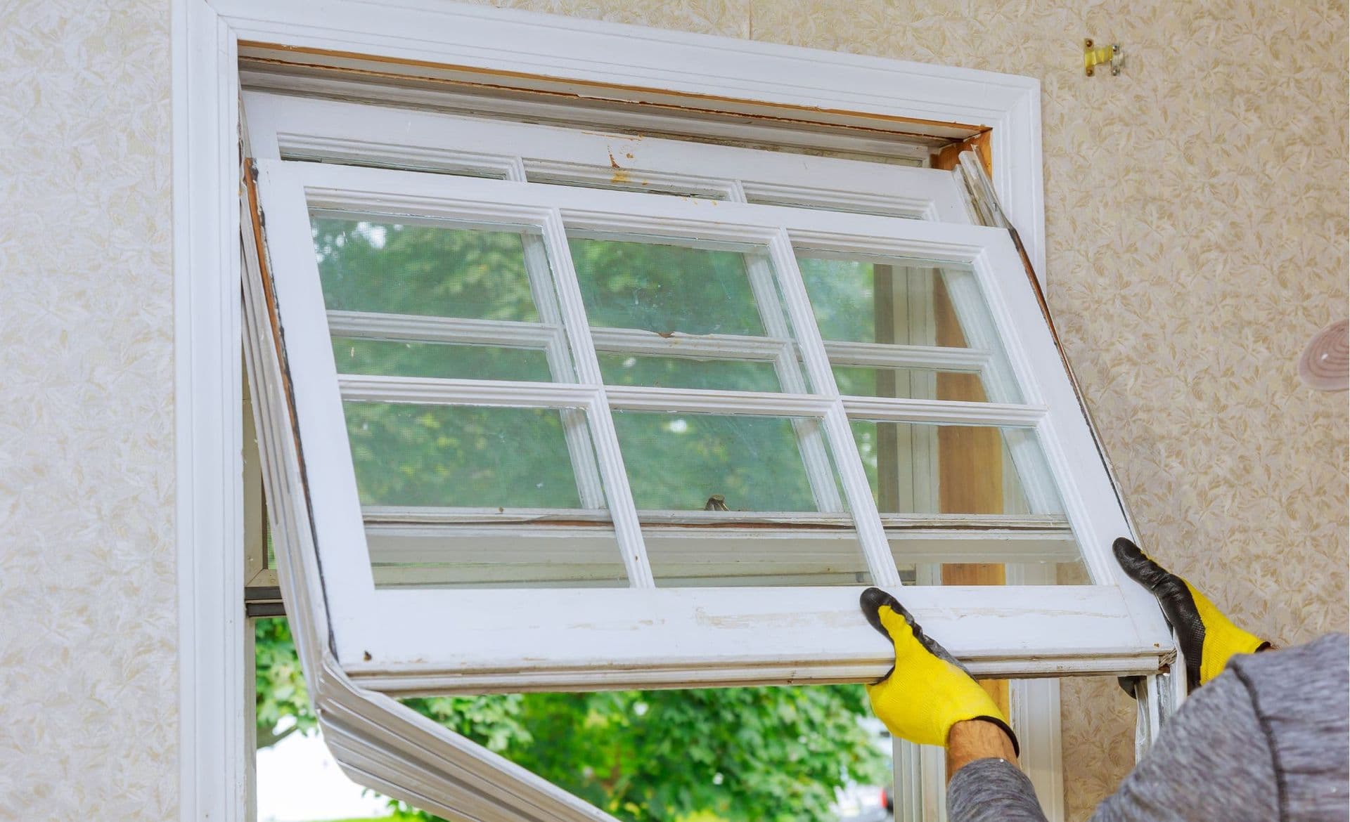 worker with yellow gloves removes old glass window from wall