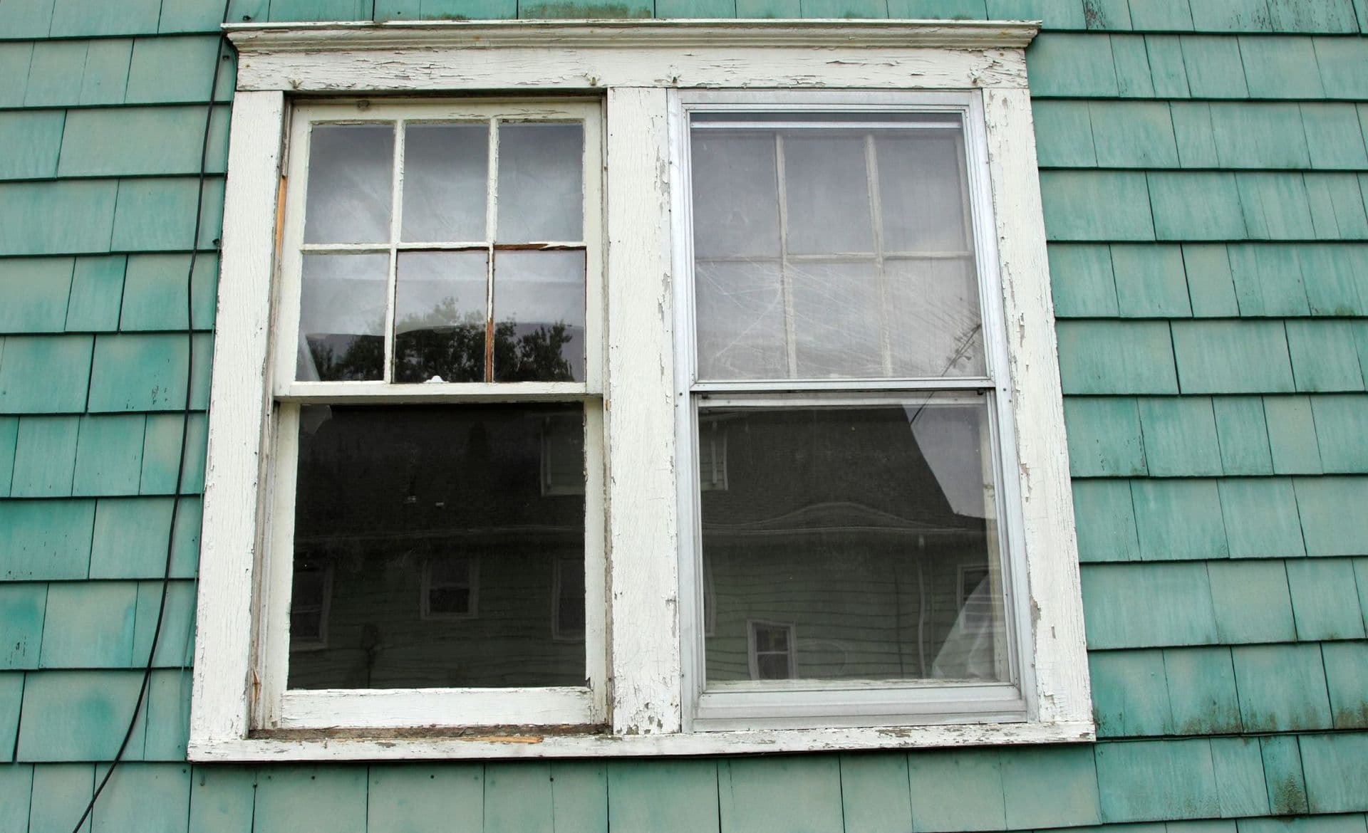 old home window with chipping paint on moss green shingled home