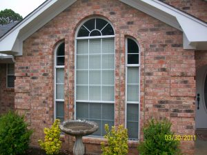 A set of large windows with an oval top on a brick-style home