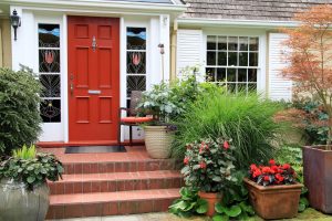 A beautiful red door with windows in a front porch area with plants and flowers